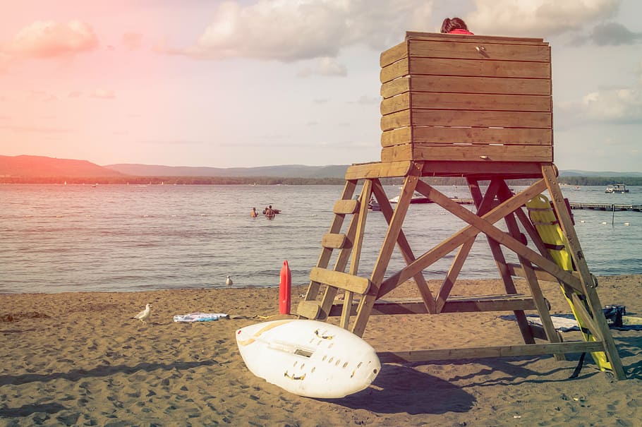 person sitting on brown wooden coast guard tower with white surfboard near beach HD wallpaper