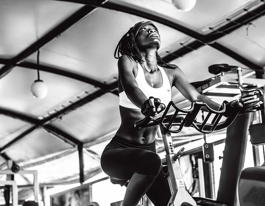 grayscale photography of woman exercising using stationary bike