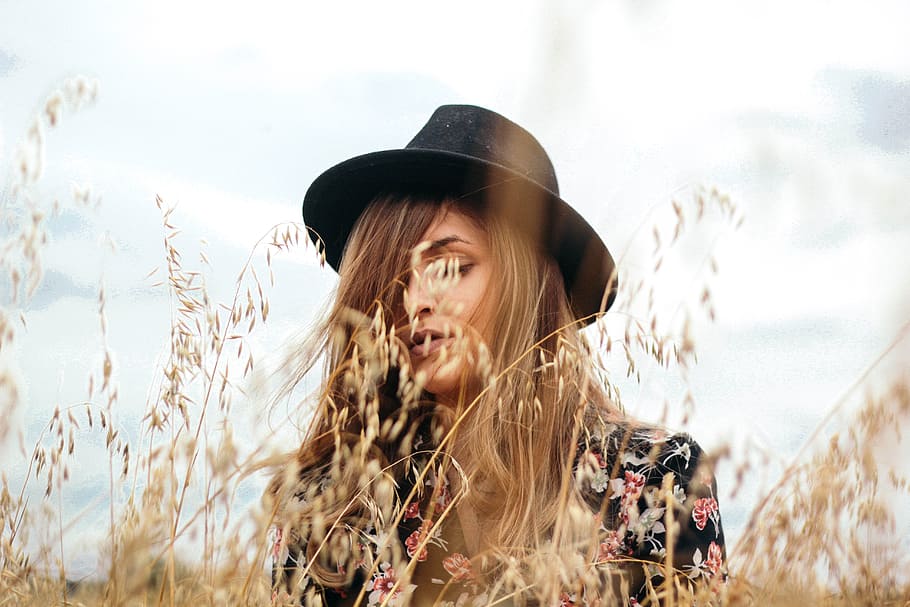 woman wearing black hat near brown grass during daytime, woman in black floral top and hat
