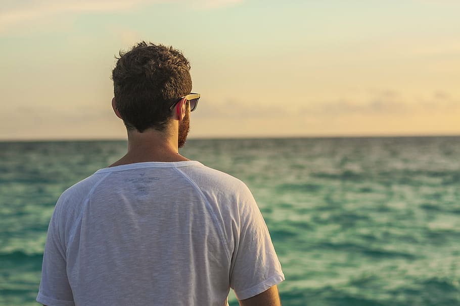 person wearing white crew-neck t-shirt while watching the body of water during daytime HD wallpaper