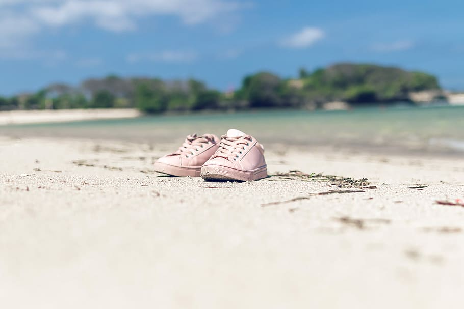 Shoes on a tropical beach of Bali island, shallow focus photography of pair of pink low-top sneakers