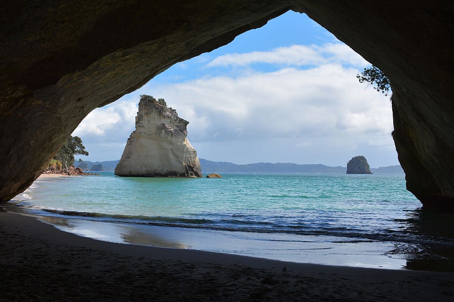 cave near seashore under blue and white sky, cathedral cove, new zealand