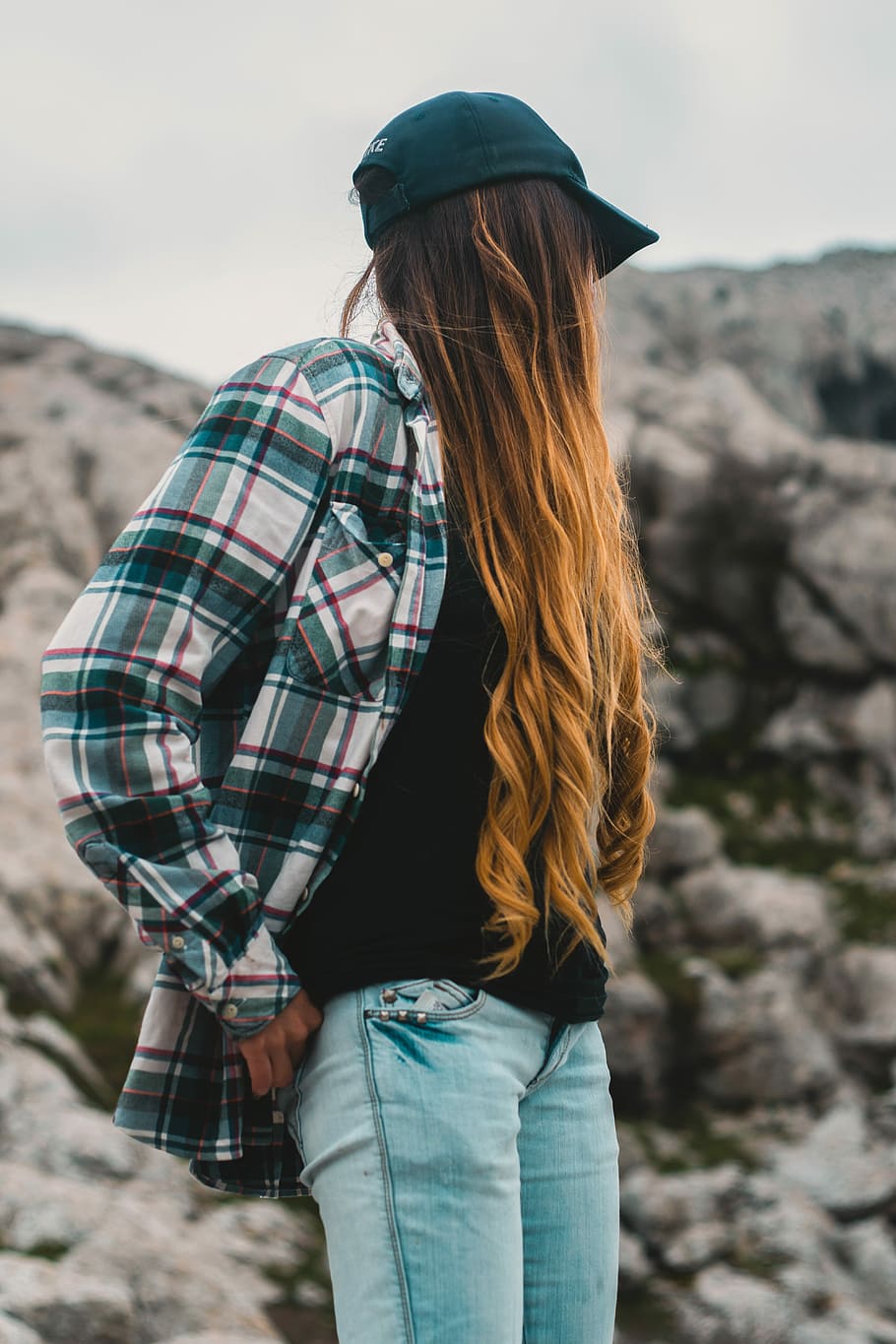 women's white, green, and black plaid dress shirt wearing green cap, selective focus of woman standing near rock formation during daytime, HD wallpaper
