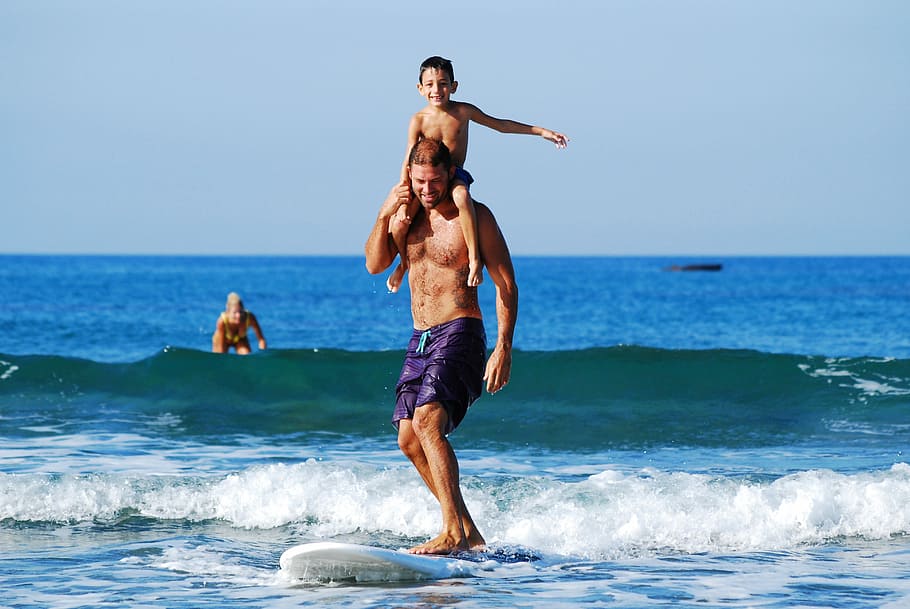 man surfboarding while lifting child, man surfing on beach, person HD wallpaper