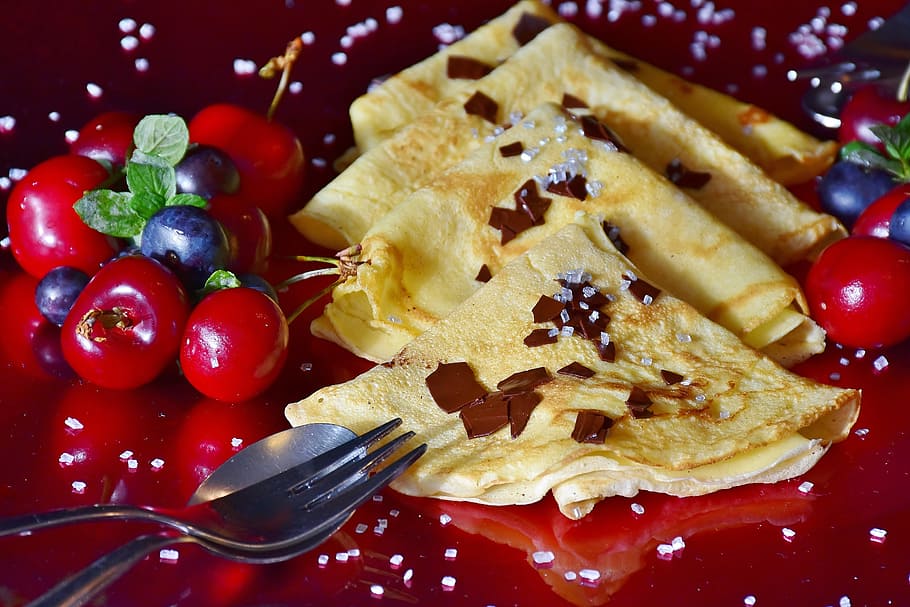 closeup photo of quesadilla beside red cherries and stainless steel spoon and fork