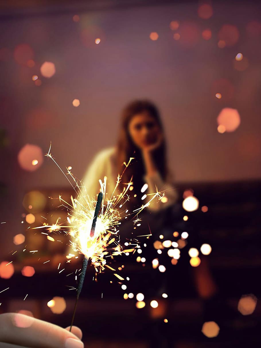 close-up photo of person holding firecracker overlooking woman sitting on chair