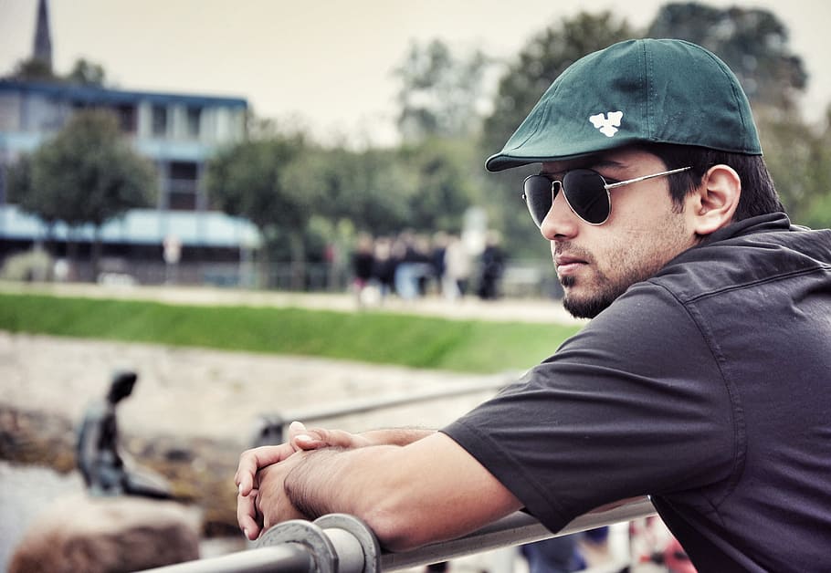 man wearing black aviator-style sunglasses leaning on gray stainless steel railings outdoor during daytime HD wallpaper