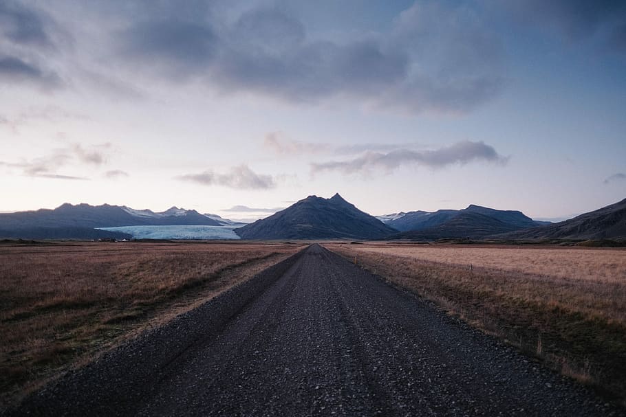 empty dirt road toward mountainous terrain under white skies HD wallpaper