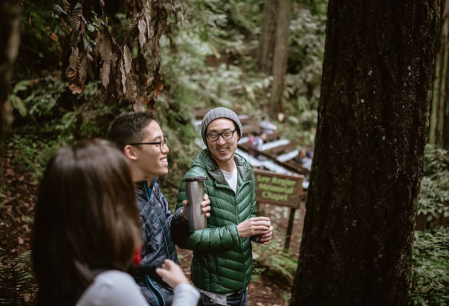 smiling two men standing surrounded by trees during daytime HD wallpaper