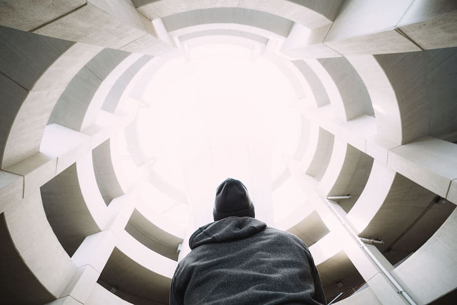 photography of person wearing gray hooded jacket inside building during daytime, low angle photography of man looking up at high-rise building HD wallpaper