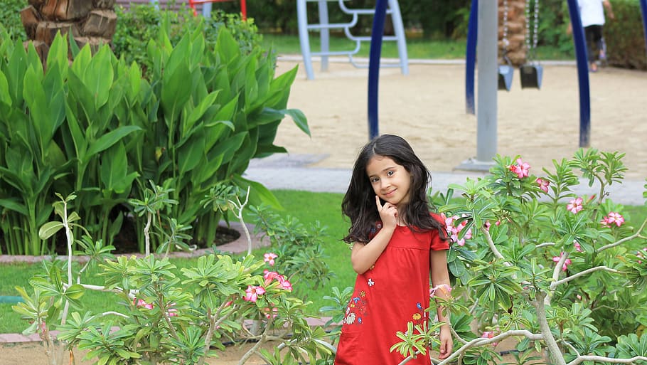 girl in red dress standing near green leafed plant during daytime