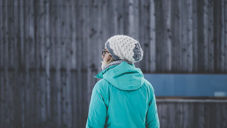 selective focus photography of woman facing wall, person wearing teal hooded jacket and white knit cap