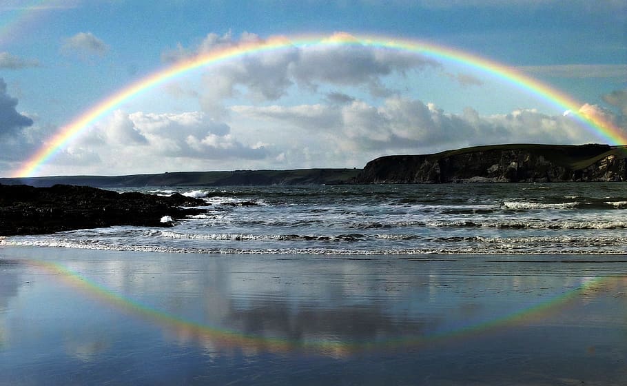 photo of rainbow reflecting on calm body of water, seaside, coast