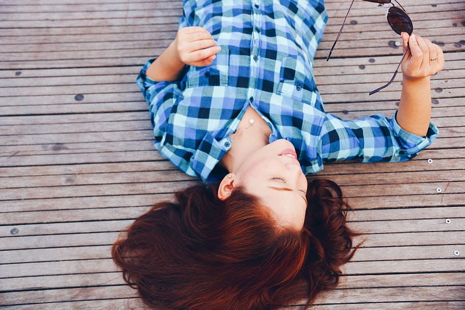 woman in blue, white, and grey plaid long-sleeve shirt lying on brown wooden surface HD wallpaper