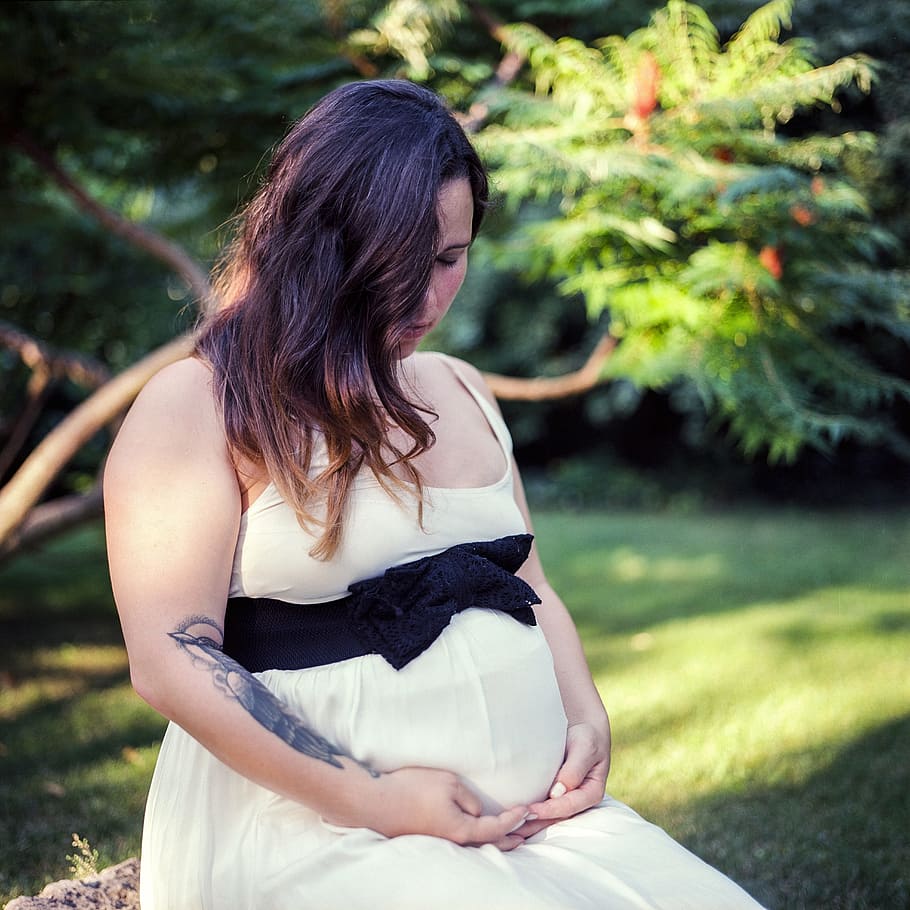 pregnant woman sitting beside grass field, garden, summer, white