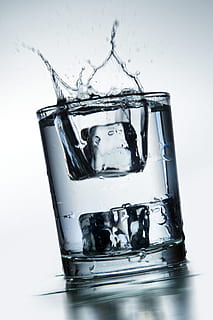clear glass filled with water and two ice cubes spilling out HD wallpaper
