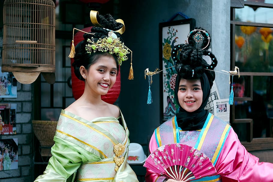 women wearing green and pink traditional dresses, two women standing on front of red paper lantern