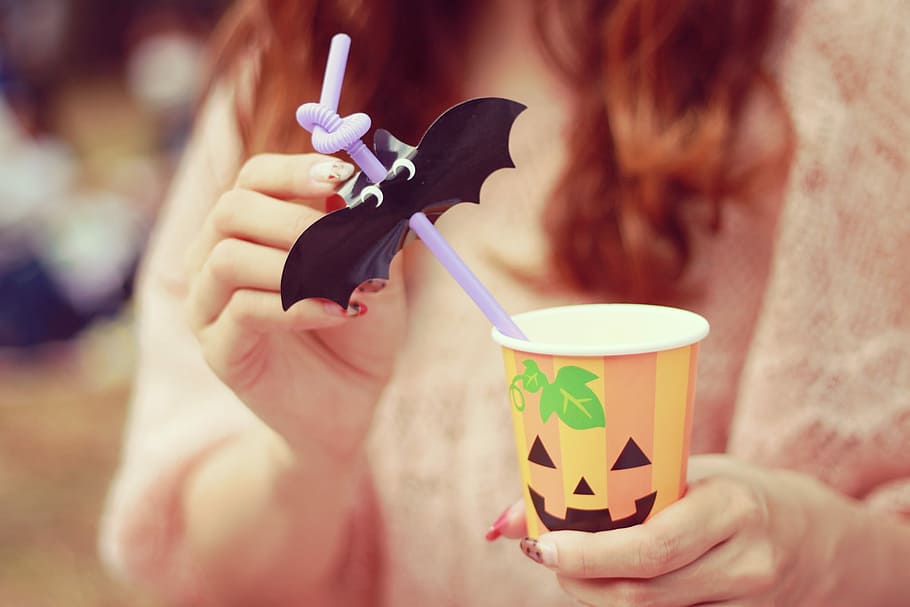 person holding a orange, white and yellow Halloween plastic cup with straw HD wallpaper