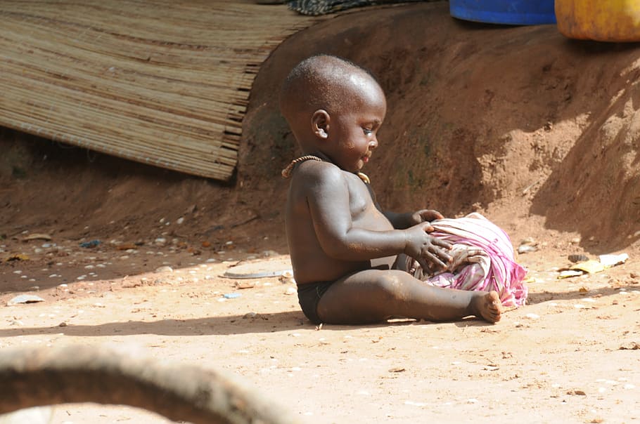 child sitting on ground holding pink textile, boy, african, small