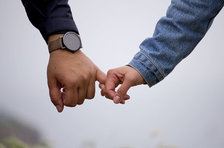 man and woman holding hands together, person holding pinky fingers in selective focus photography