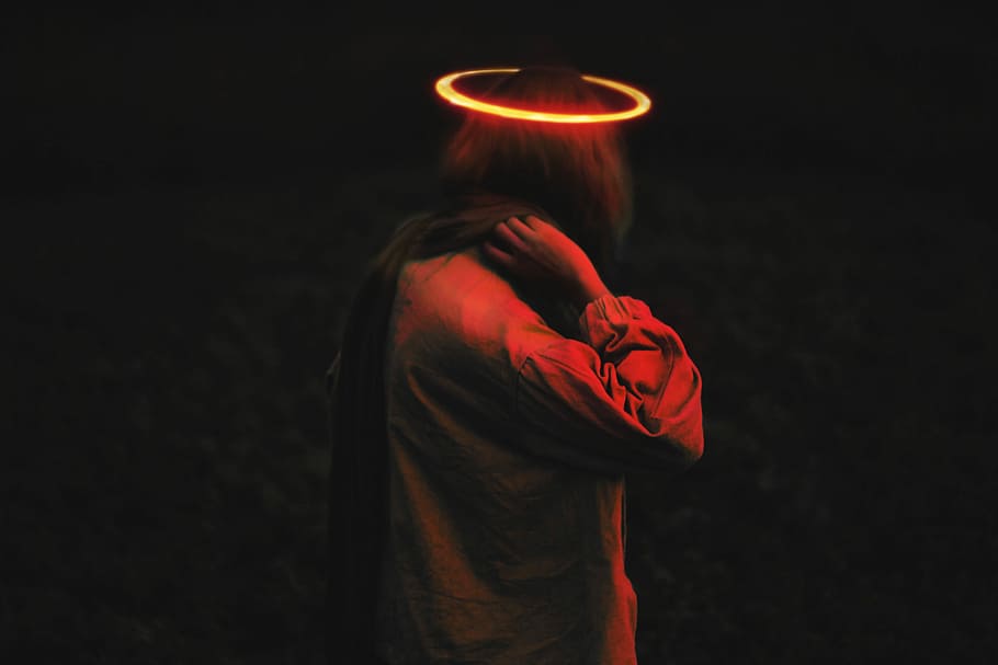 person wearing long-sleeved top with halo, person with hands on nape in dark lit room