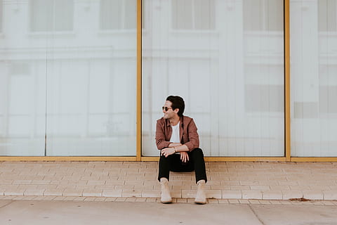 photo of man sitting on brown bricks against glass wall, man in brown suit jacket with pants and brown boots outfit sitting beside clear glass framed window HD wallpaper