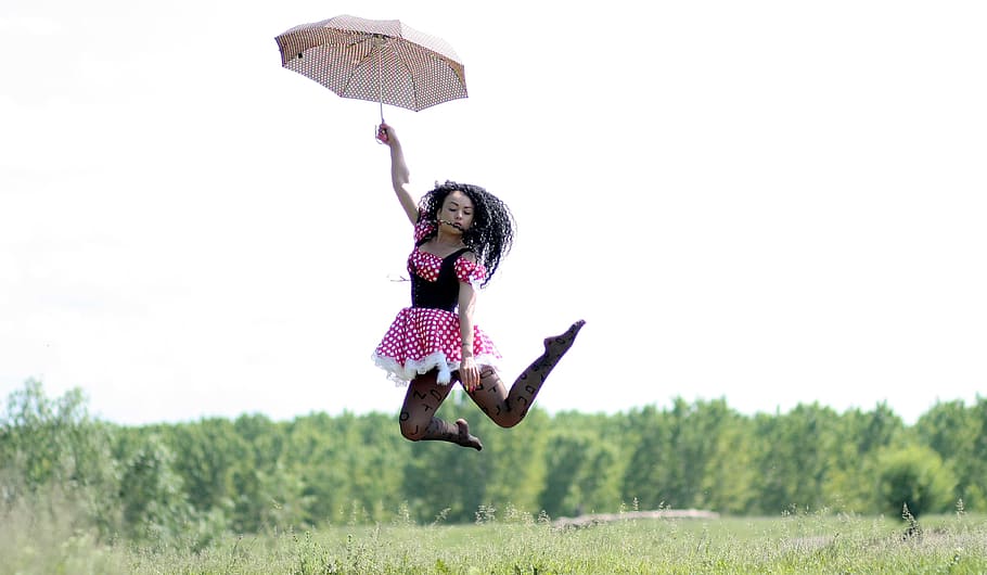 woman holding brown umbrella jump in the air with green trees as background, HD wallpaper