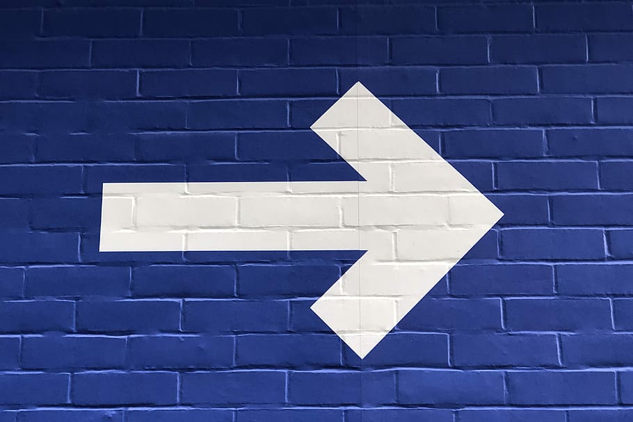 white arrow painted on brick wall, blue wall with white painted arrow pointing on right direction