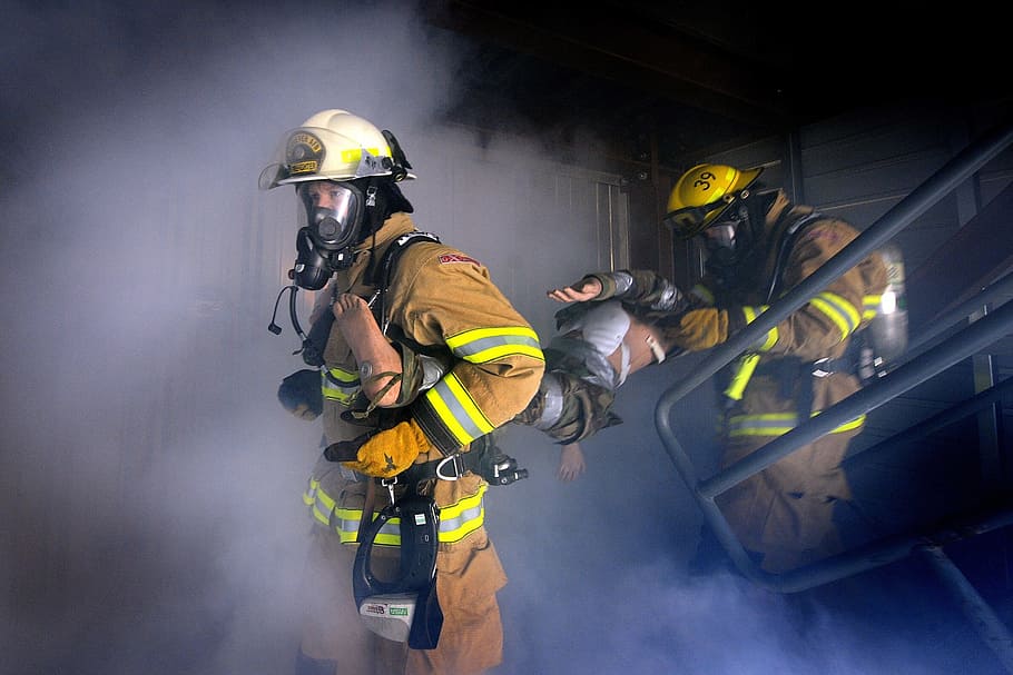 two firemen carrying a man inside dark room covered with smoke