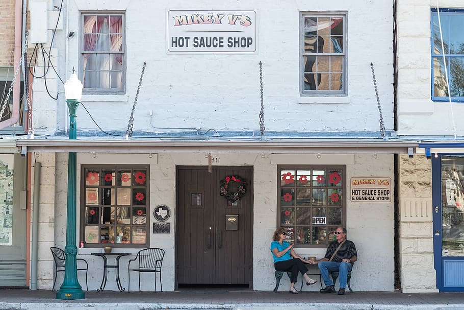 man and woman sitting in front of Hot Sauce Shop storefront, man and woman sitting together outside the Mikey V's hot sauce shop HD wallpaper