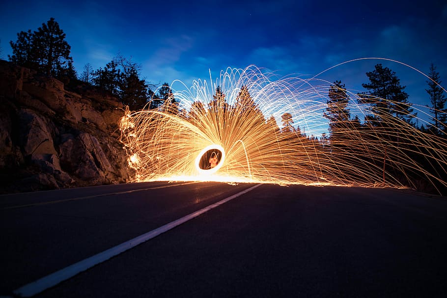 time lapse photography of fire dancing, steel wool photography of person near rock formation under blue sky during nighttime