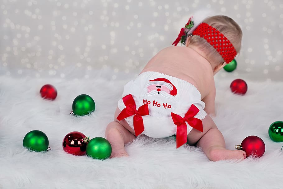 baby in white diaper playing green and maroon baubles, christmas