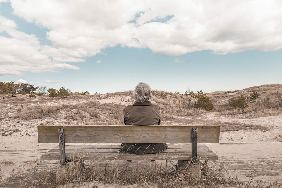 person sitting on bench, man wearing grey vest sitting on bench under white cloudy sky during daytime HD wallpaper
