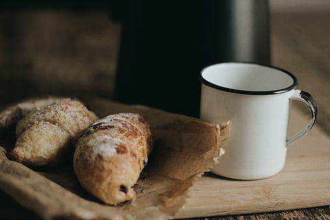 two breads on paper bag beside cup, shallow focus photography of pastry on paper bag HD wallpaper