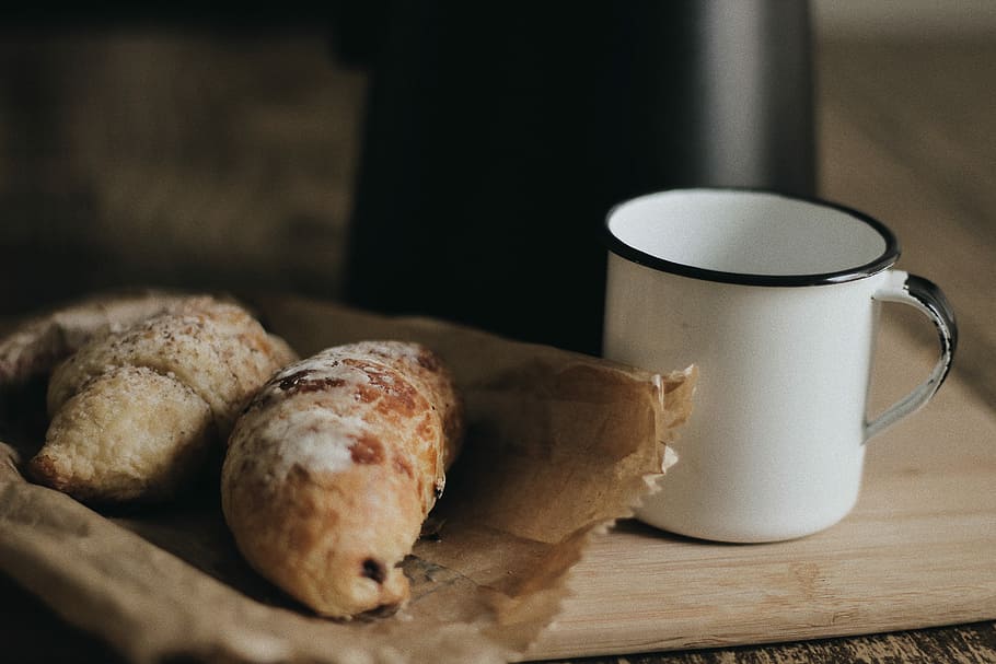 two breads on paper bag beside cup, shallow focus photography of pastry on paper bag HD wallpaper