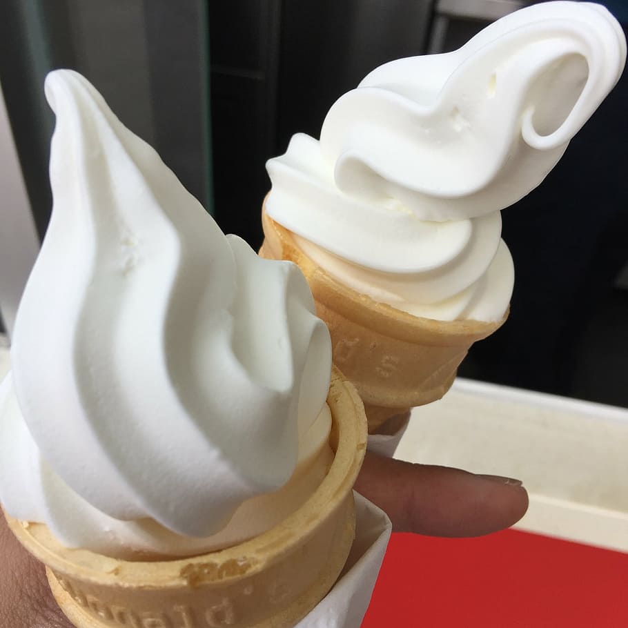 person holding two vanilla ice creams, cones, whipped ice cream