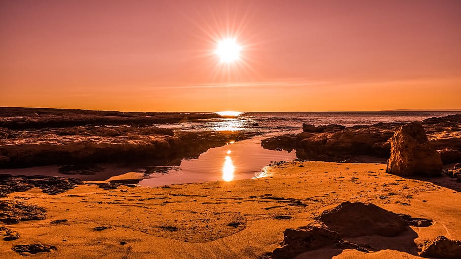 silhouette photography of rock near body of water at golden hour HD wallpaper