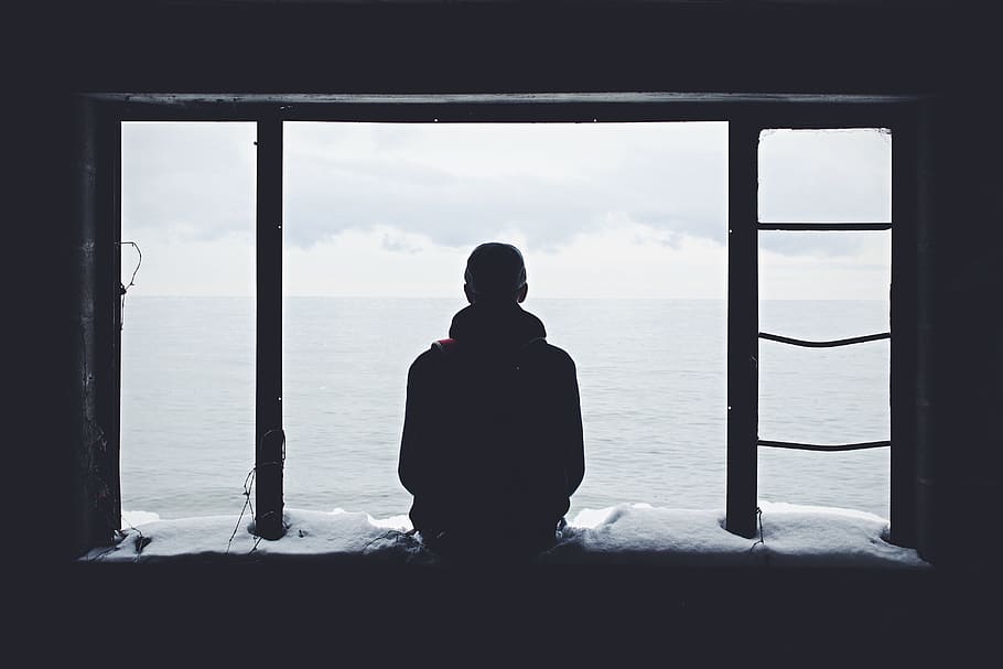 silhouette of person sitting on window in front of sea during daytime HD wallpaper