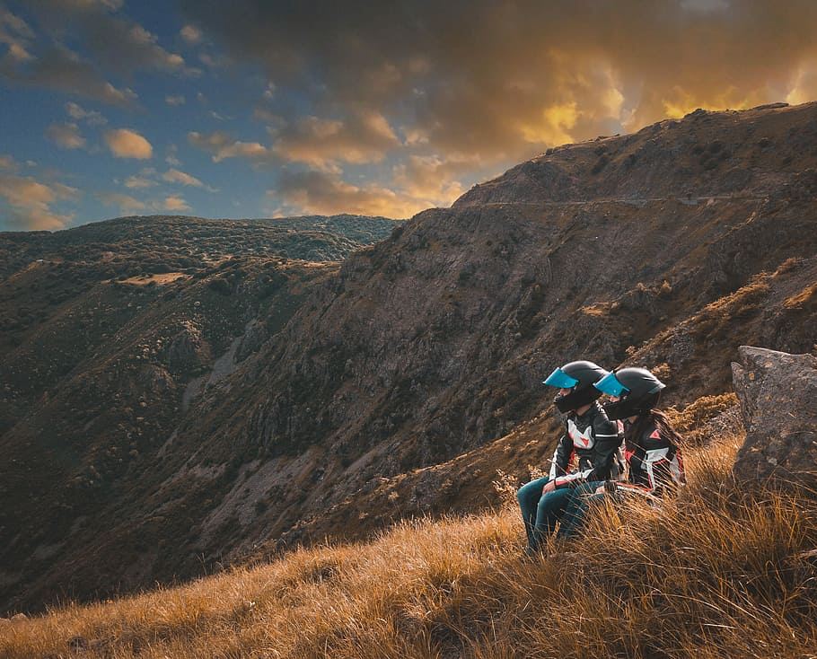 two person's sitting on grass overlooking mountains during golden hour