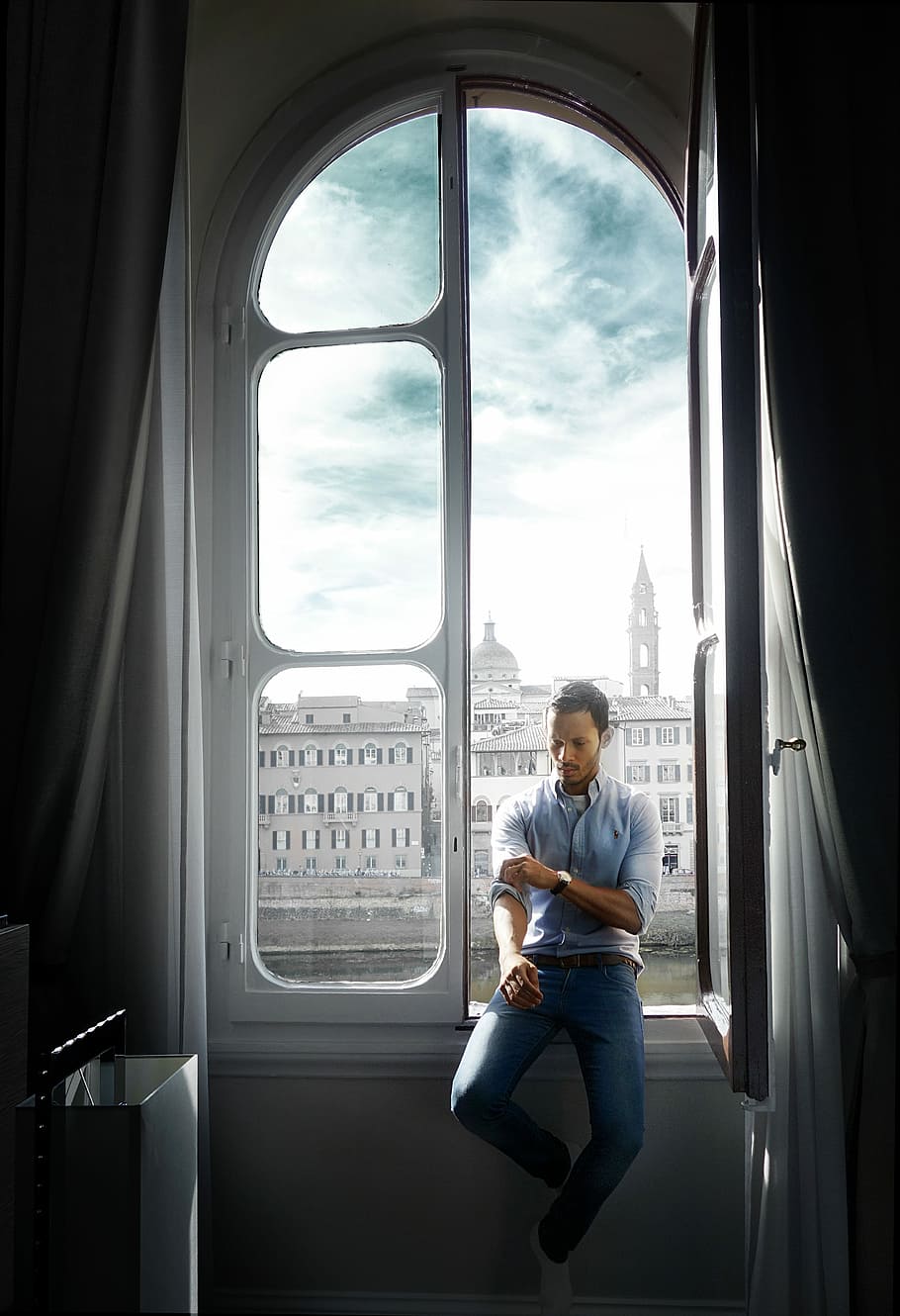 man sitting on window during daytime, man sitting on window fixing his sleeve with building background HD wallpaper