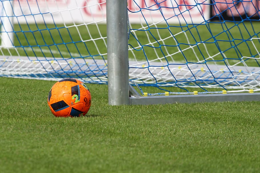 orange and black soccer ball beside soccer goal on soccer field