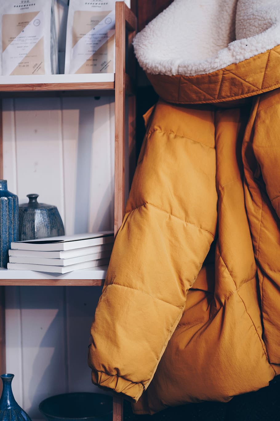 hang brown bobble coat beside book, orange parka jacket hanging beside shelf HD wallpaper