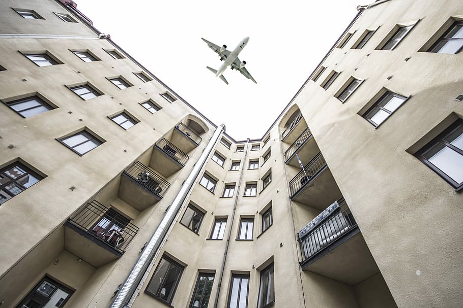 worm's-eye view photography of building and airplane, low angle photo of white commercial plane flying over white building during daytime HD wallpaper
