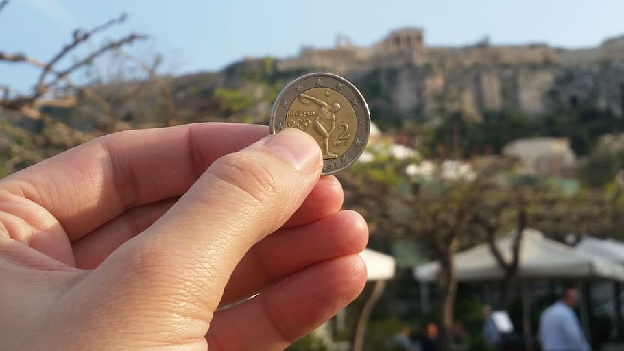 person holding round silver-and-gold colored coin, acropolis