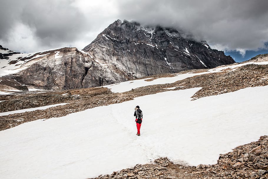 person walking on snow towards mountain, person walking on snow covered ground overlooking grey mountain HD wallpaper