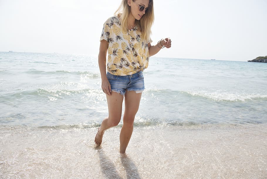 photo of woman wearing brown, gray ,and black floral top and blue short shorts walking in seashore HD wallpaper