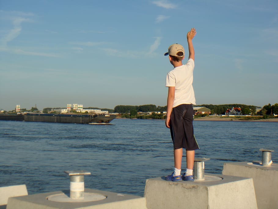 boy standing on concrete block waving on ship at daytime]\ HD wallpaper