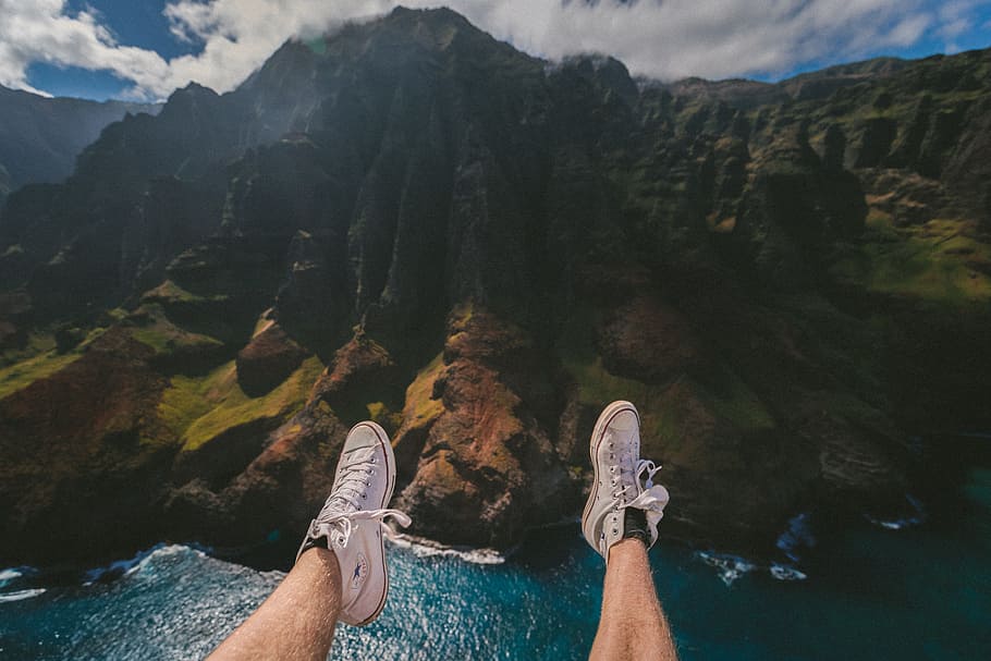 person above mountain and body of water, photo of person wearing white sneakers
