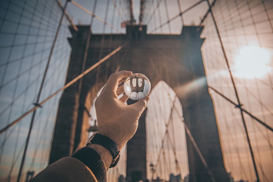 man holding ball facing Brooklyn Bridge, New York, person holding lens front of Brooklyn Bridge HD wallpaper