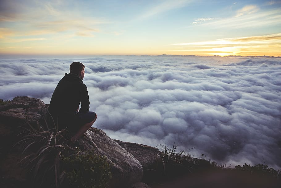 man sitting on rock facing cloudy during daytime, top, mountain